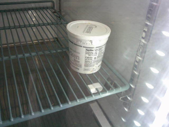 Tub of chicken base on shelf of a fridge.